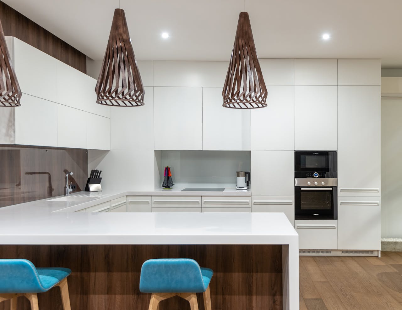 heros-img Turquoise chairs at counter with white cupboards and modern kitchenware in spacious light kitchen with hanging lamps in contemporary apartment